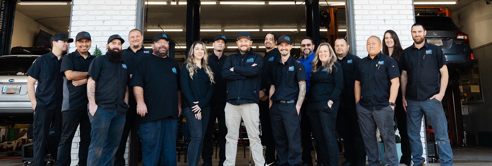 Group photo of the Car Doctors team standing in front of an open shop bay with cars on lifts in the background.