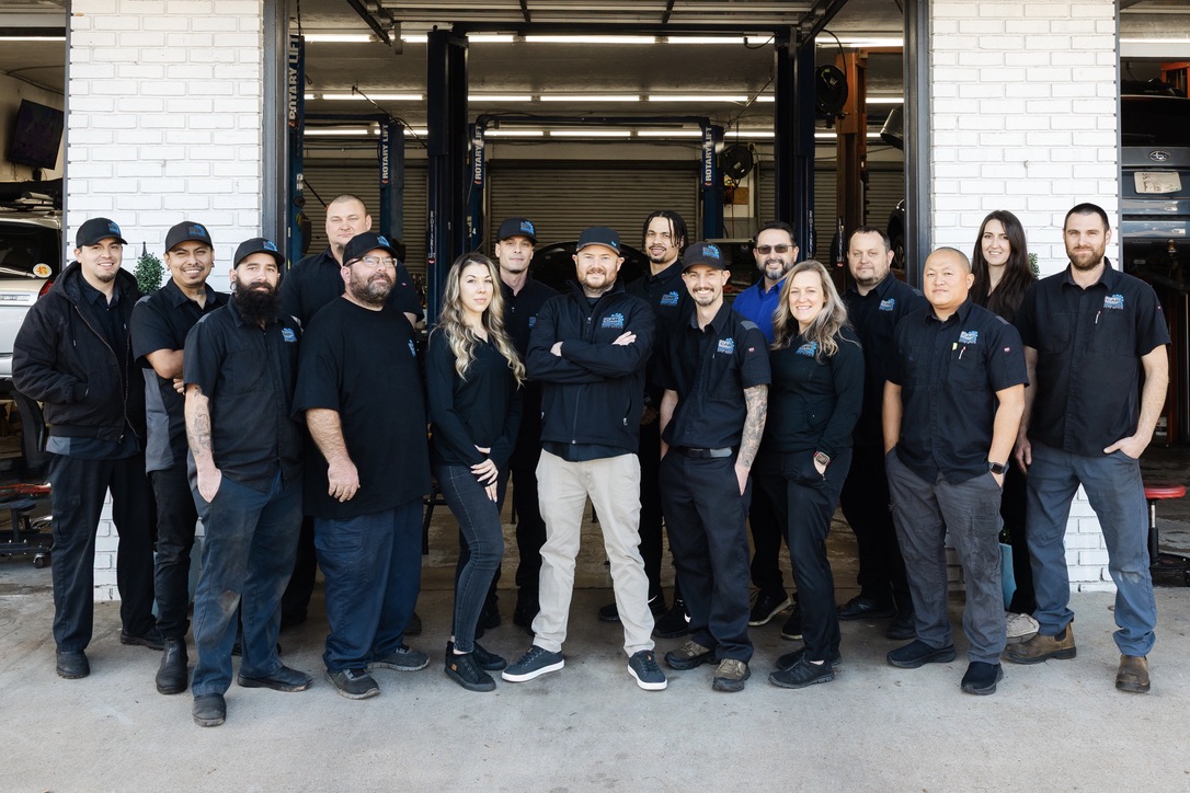 Group photo of the Car Doctors team standing in front of an open shop bay with cars on lifts in the background.